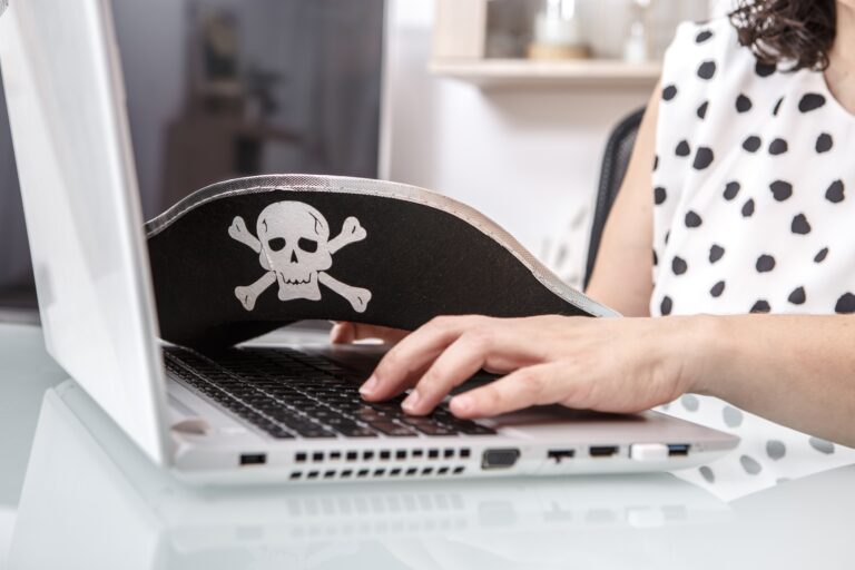 A person engages in online activities in a workspace, wearing a pirate-themed hat with a skull and c