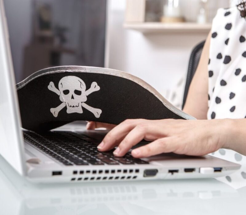 A person engages in online activities in a workspace, wearing a pirate-themed hat with a skull and c