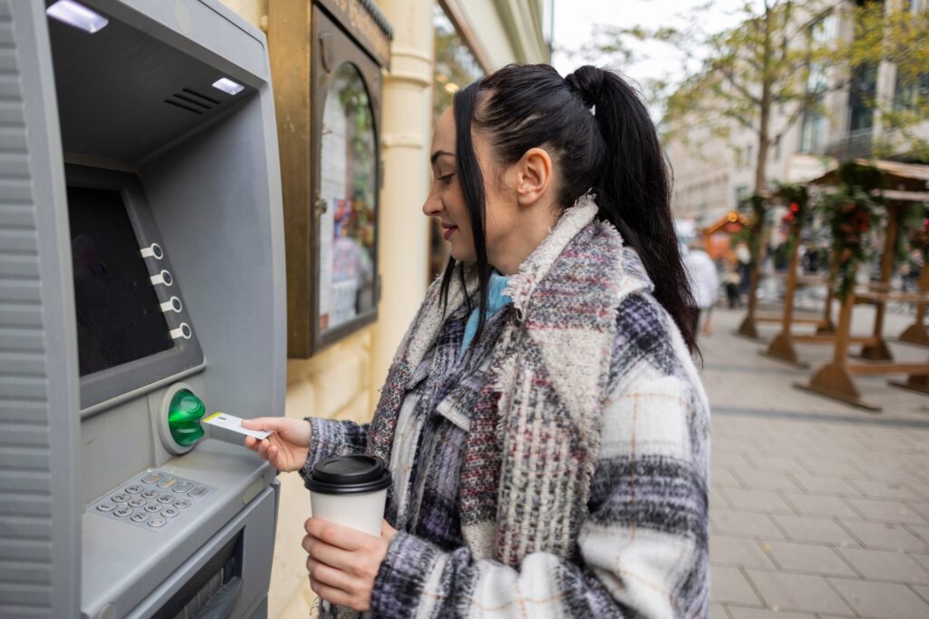 Woman Using ATM on City Street with Coffee in Hand