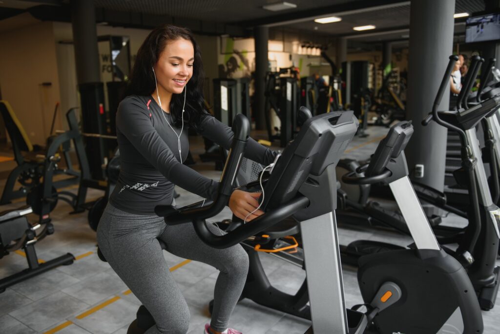 Young woman with headphones doing exercises on stationery bicycle in a gym or fitness center