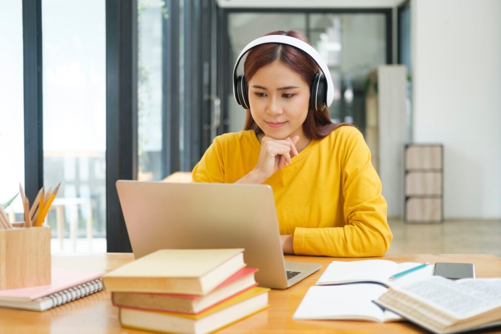 Young woman studying or working online using laptop and wearing headphones.